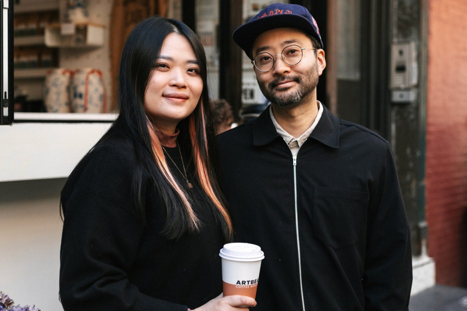 Image of Khanh and Spencer standing in front of Artbean Coffee with Khanh holding a coffee cup
