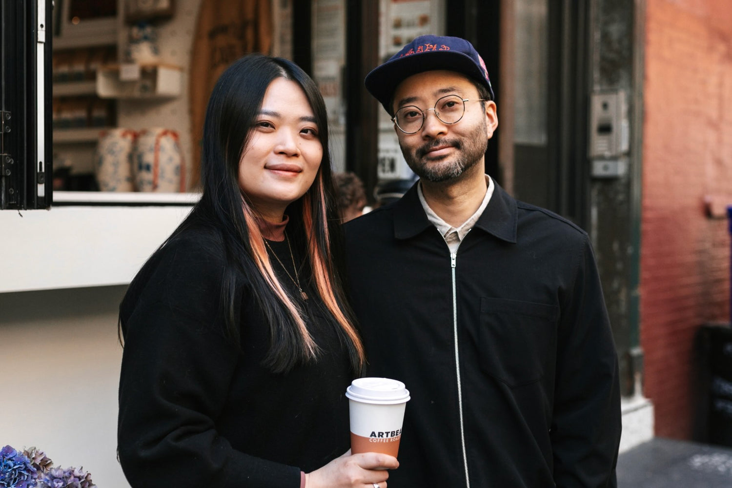 Image of Khanh and Spencer standing in front of Artbean Coffee with Khanh holding a coffee cup